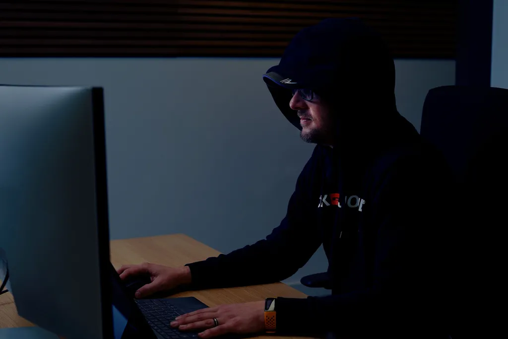 Person mit dunkler Kapuze arbeitet an Computer in dunklem Raum, symbolisiert Hacker