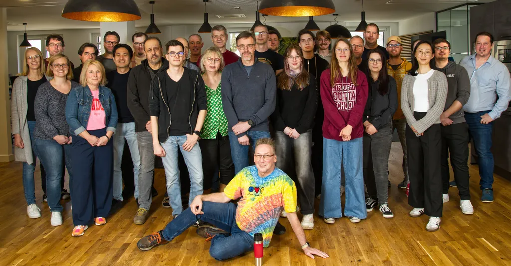 Das cycos-Team steht (und eine Person sitzt) zusammen in der Lounge des Büros