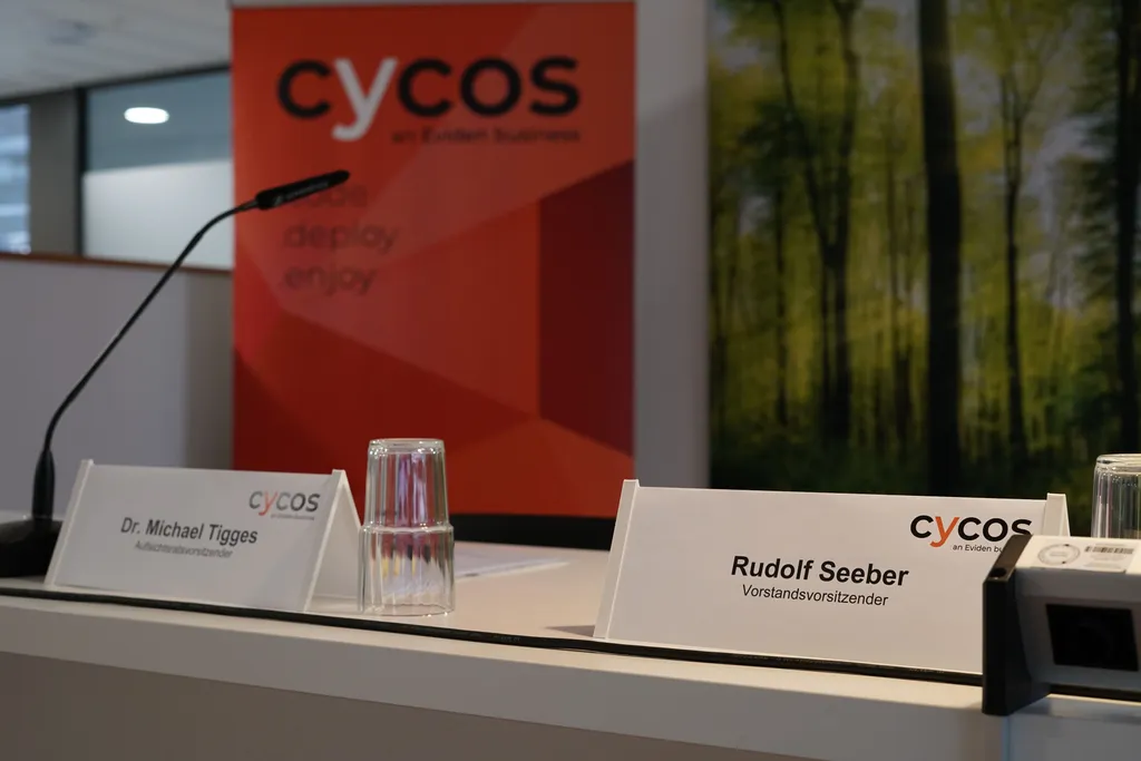 Tisch unserer Hauptversammlung mit Mikrofonen, Namensschildern und Markenbanner im Hintergrund.